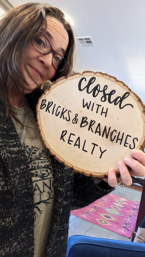 Courtney Hedrick Edmond Realtor with a Bricks and Branches Realty Holding Wood Closing Sign