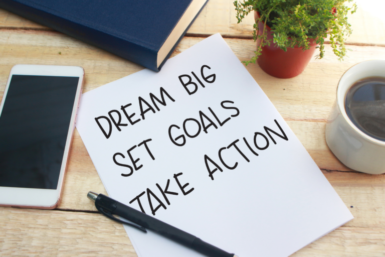 dream framework paper on a desk that reads dream big set goals take action with a book and a plant